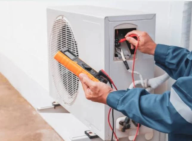 Close-up of a technician testing condenser components with an orange multimeter