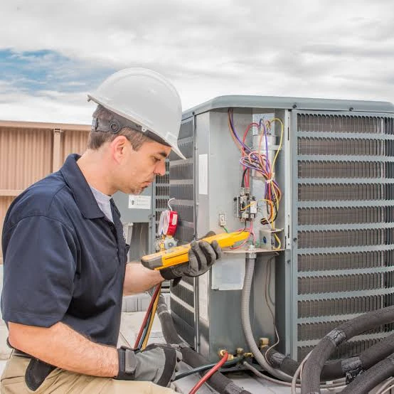HVAC technician using a diagnostic meter beside an open outdoor air-conditioning unit