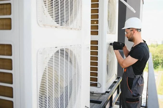 Technician using a drill to work on large outdoor air-conditioning units